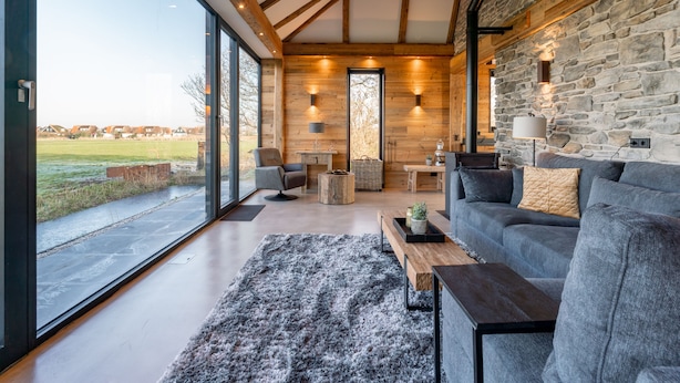 A modern living room with a stone wall, large windows, and a cozy fireplace. - Unique villa with fantastic views, near the beach (Callantsoog)