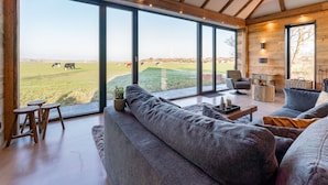 A spacious living room with a large window overlooking a green field and cows. - Unique villa with fantastic views, near the beach (Callantsoog)