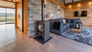 A modern living room with a stone wall, wooden beams, a fireplace, a sofa, and a TV mounted on the wall. - Unique villa with fantastic views, near the beach (Callantsoog)