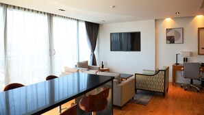 Een moderne hotelkamer met een eethoek, een bank, een aan de muur bevestigde televisie en een bureau met een lamp.