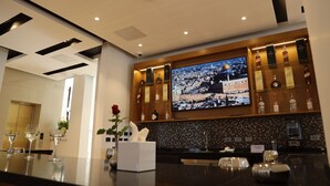 Een moderne bar met een groot flatscreen waarop een stadsgezicht te zien is, drankflessen op de planken en een bargedeelte met glazen en een bloevas.
