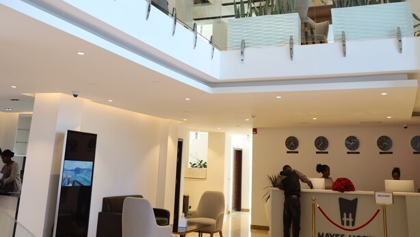 Een hotel lobby met een receptiebalie, een zithoek en een trap naar een hoger gelegen verdieping.