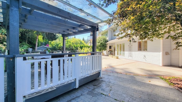 A covered outdoor area with a white railing, a paved walkway, and a house in the background. - Ocean Park B&B (Surrey)