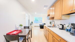 A modern kitchen with wooden cabinets, a dining area with a table and chairs, and a window providing natural light. - Ocean Park B&B (Surrey)