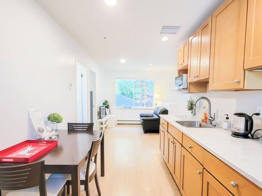 A modern kitchen with wooden cabinets, a dining area with a table and chairs, and a window providing natural light.