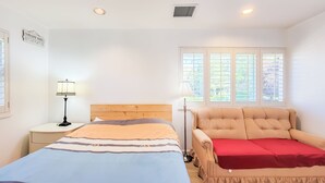 A bedroom with a bed, a chair, a nightstand, a lamp, and a window with blinds. - Ocean Park B&B (Surrey)