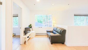 A modern living room with a leather sofa, a TV on a white stand, and a small table with a plant. - Ocean Park B&B (Surrey)