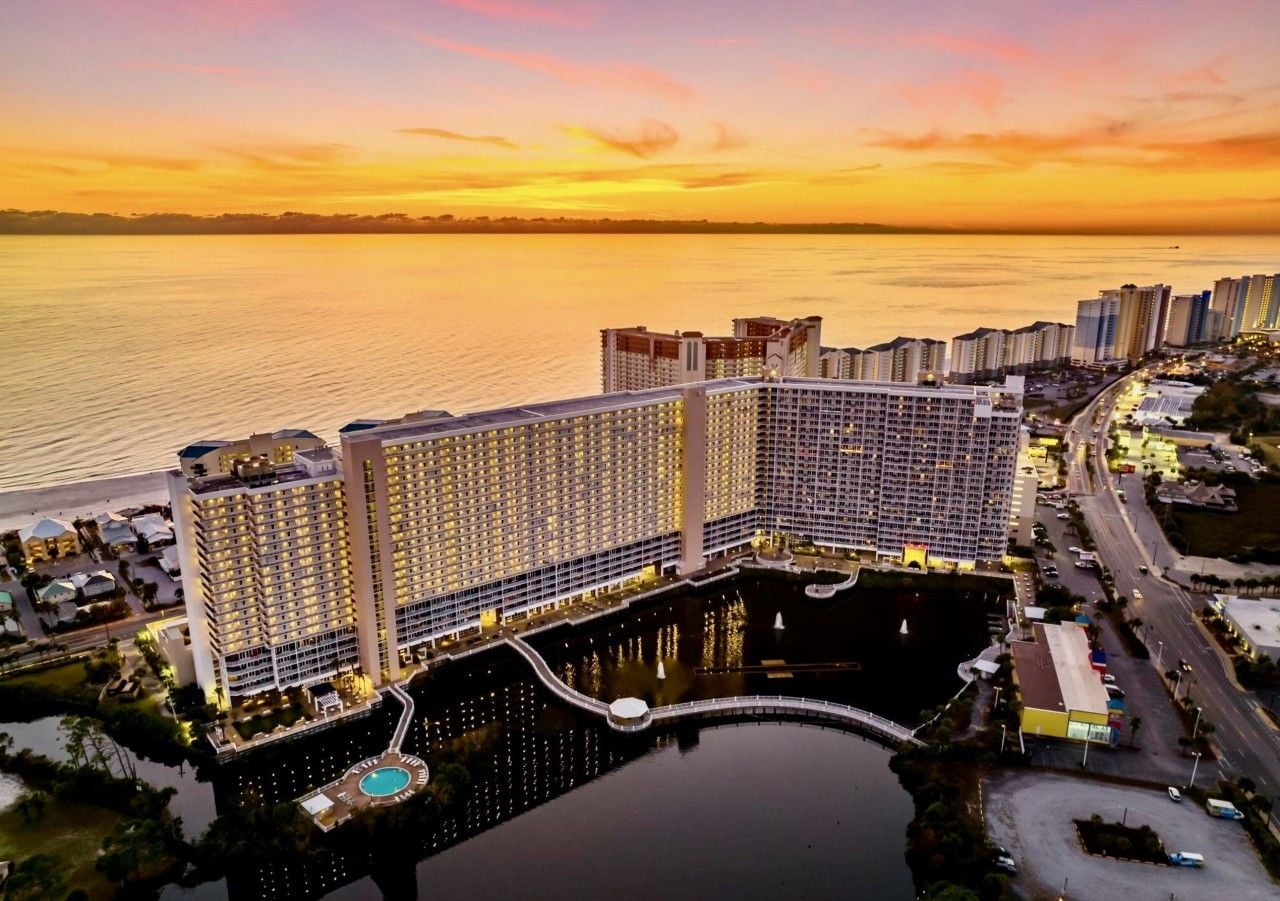 A high-rise hotel with multiple floors, a central courtyard, and a body of water in the foreground.
