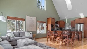 Un vaste espace de vie comprenant un grand canapé, une table à manger avec des chaises, et une cuisine dotée de meubles en bois et d’un réfrigérateur en acier inoxydable.