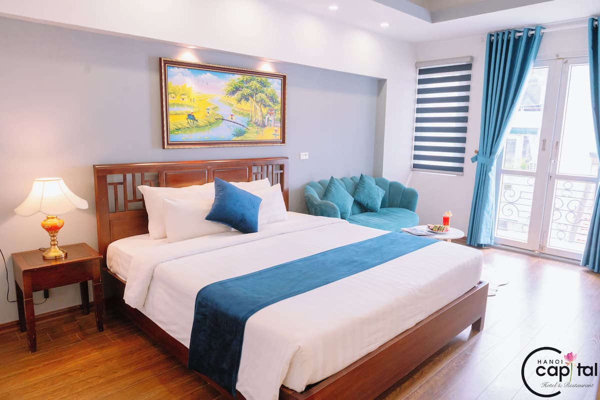 Une chambre d’hôtel avec un grand lit, une table de chevet avec une lampe, un tableau au mur, une fenêtre avec des rideaux et une vue sur l’extérieur.