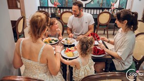 Una familia cenando en un restaurante con decoración tradicional, que incluye sillas de ratán y un mural floral en la pared.