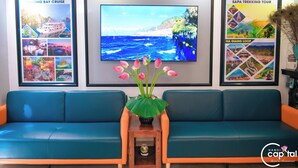 Zona de recepción con un sofá azul, un televisor mostrando una escena costera y carteles de viajes enmarcados.