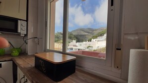 Une cuisine dotée d’un plan de travail en bois, d’un four à micro-ondes et d’une fenêtre offrant une vue sur des immeubles et des collines.