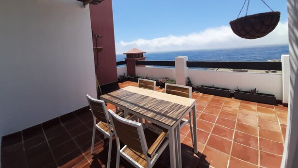 Une terrasse avec une table et des chaises, donnant sur la mer.