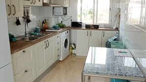 Une cuisine moderne avec des meubles blancs, un lave-linge, un four à micro-ondes et une table à manger avec un tabouret bleu.