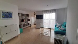 Un salon moderne avec un canapé de couleur turquoise, une table basse en verre, un téléviseur et une bibliothèque.