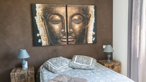 Een slaapkamer met een groot boeddhabeeld, twee nachtkastjes met lampen, gestreepte kussens en een opgemaakt bed.