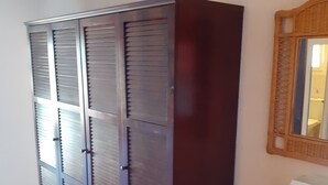 Una habitación con un armario grande, una mesita con lámpara y un espejo en la pared.
