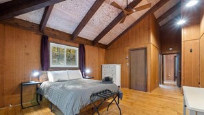 A wooden-paneled bedroom with a bed, bedside lamps, a dresser, and a window with curtains.