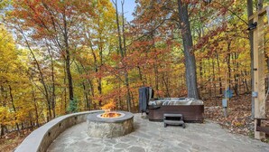 A stone fire pit and a hot tub in a forested area.