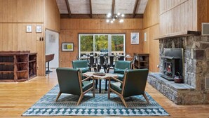 A cozy interior with wooden walls, a stone fireplace, and a dining area with green chairs.