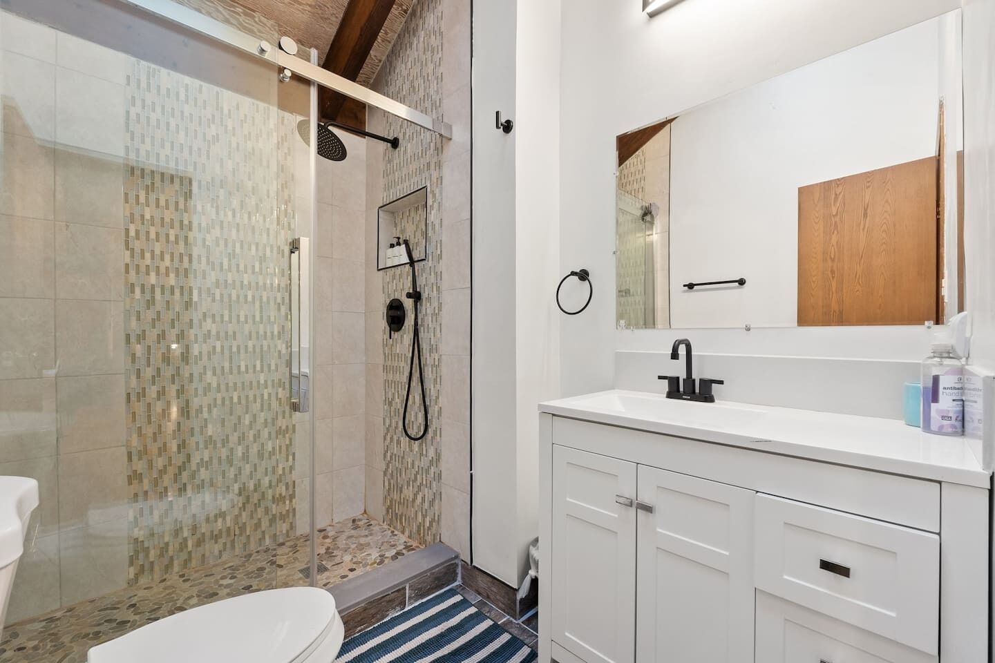 A modern bathroom with a glass-enclosed shower, a white sink, and a wooden cabinet.
