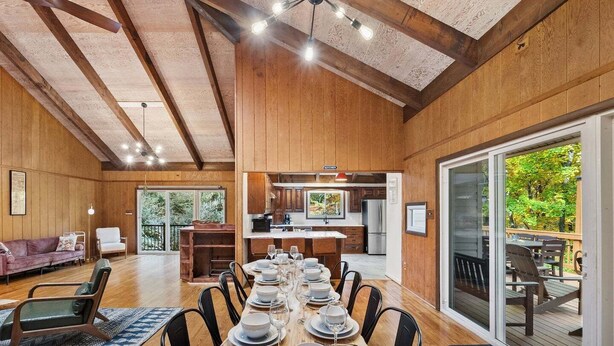 A spacious dining area with a long wooden table set for a meal, a kitchen in the background, and a large sliding glass door leading to an outdoor deck.