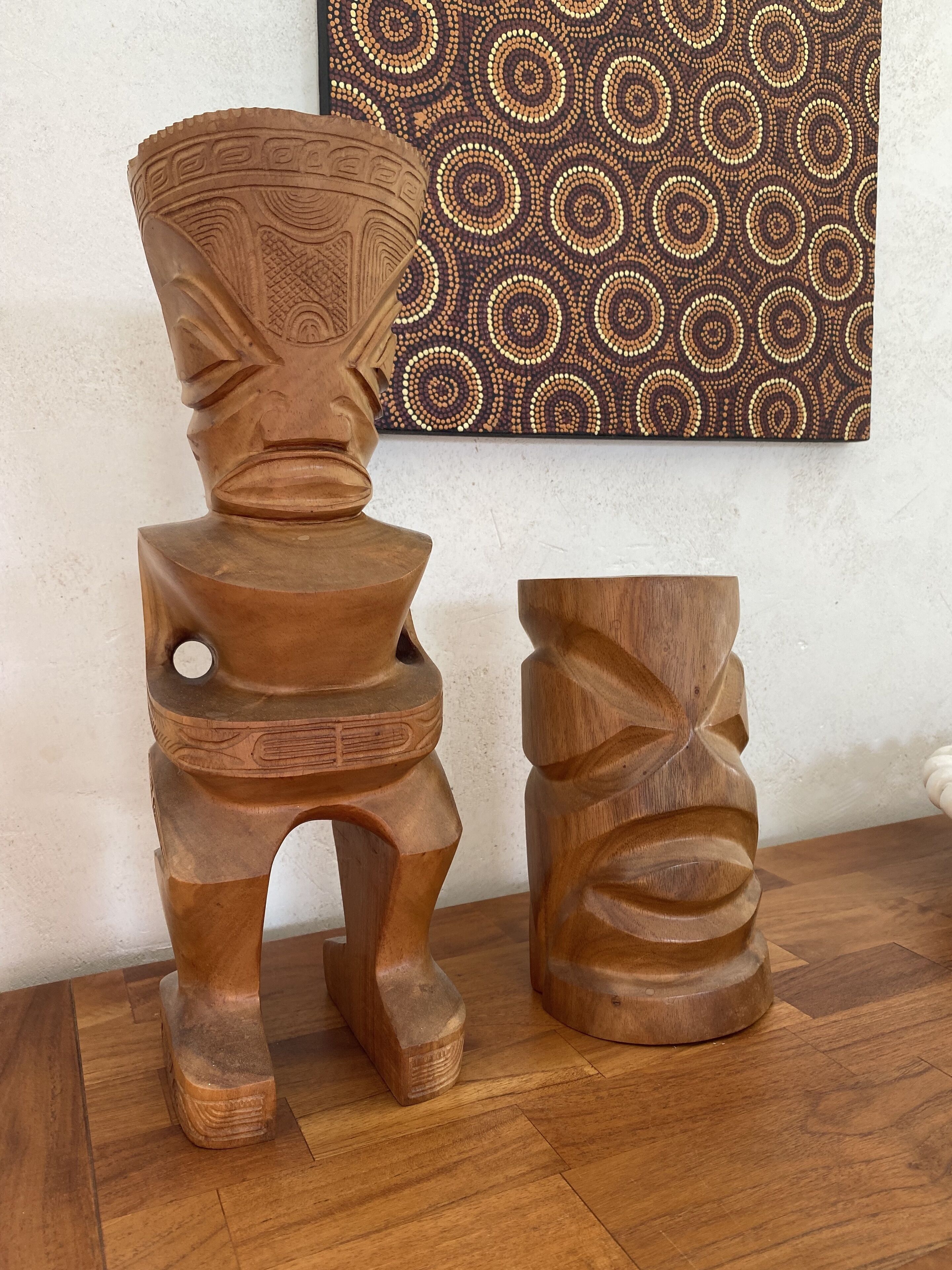Deux sculptures en bois, posées sur un plancher en bois, avec un mur à motifs en arrière-plan.