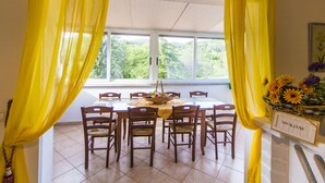 Un coin repas avec une table dressée pour six personnes, entourée de chaises, avec une vue sur l’extérieur grâce à une fenêtre et des rideaux jaunes.