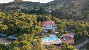 Une grande maison avec une piscine, entourée d’une végétation luxuriante et avec des collines en arrière-plan.