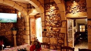Una habitación con paredes de piedra, un televisor montado en la pared, una mesa con mantel floral y un árbol de Navidad en la esquina.