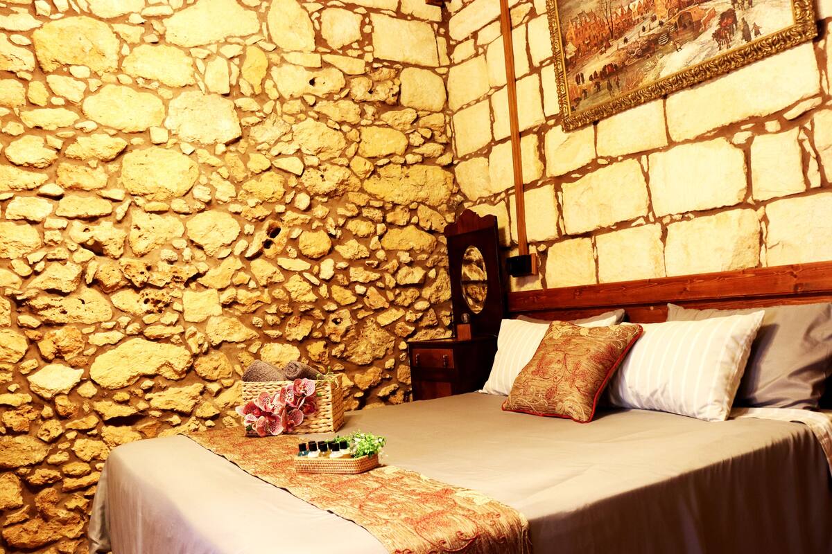 Una habitación con pared de piedra, estructura de cama de madera y un cuadro sobre la cama.