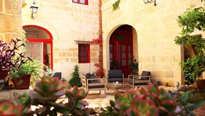 Un patio con paredes de piedra, ventanas de marco rojo y mobiliario para exteriores.