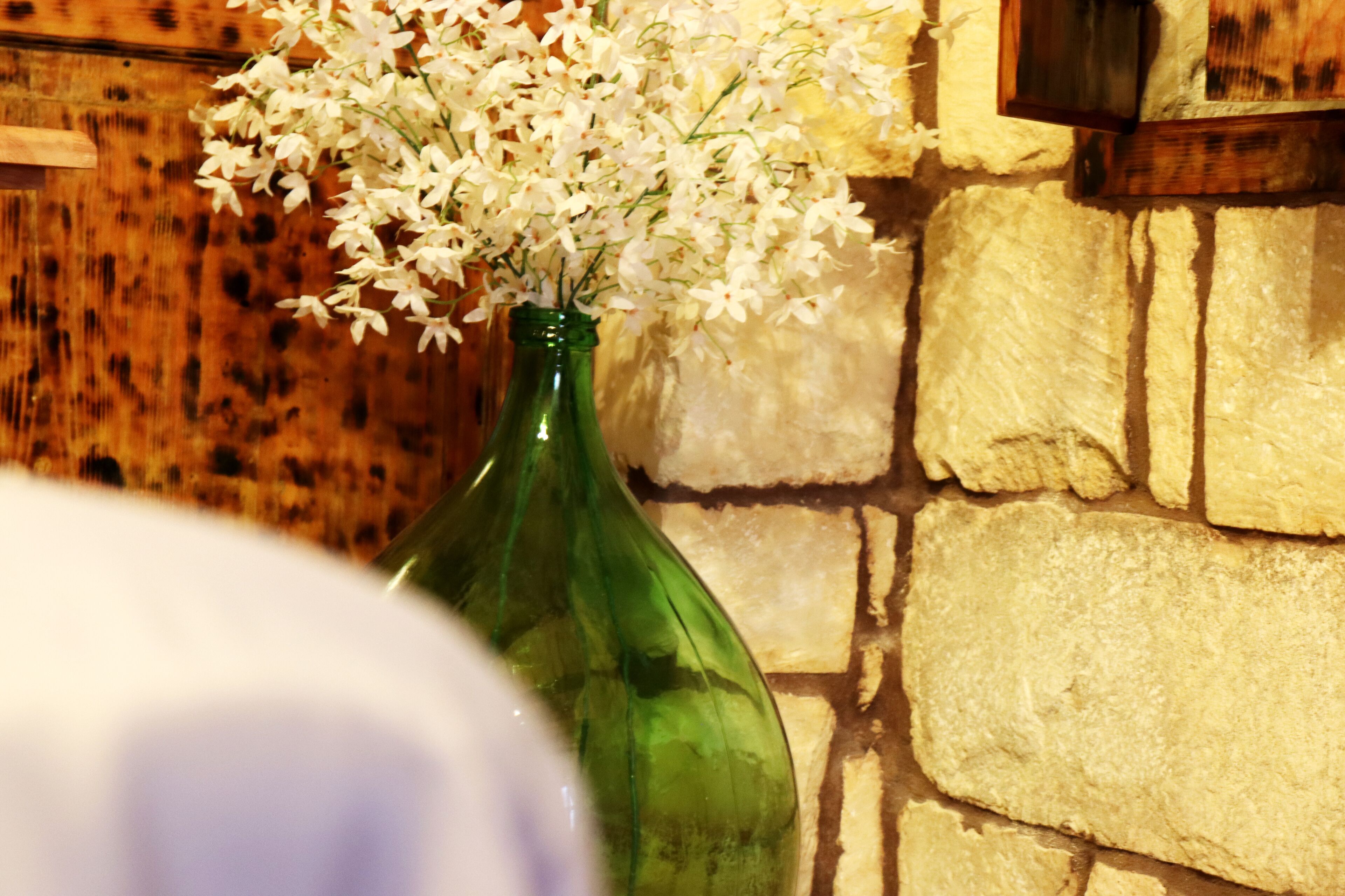 A green glass vase with white flowers against a stone wall.
