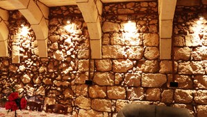 Una habitación con paredes de piedra, vigas de madera, una mesa con mantel floral y una silla.