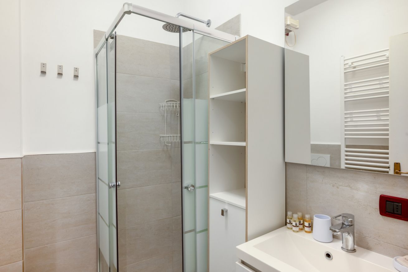 A modern bathroom with a glass shower enclosure, a white sink with toiletries, and a mirror above the sink.