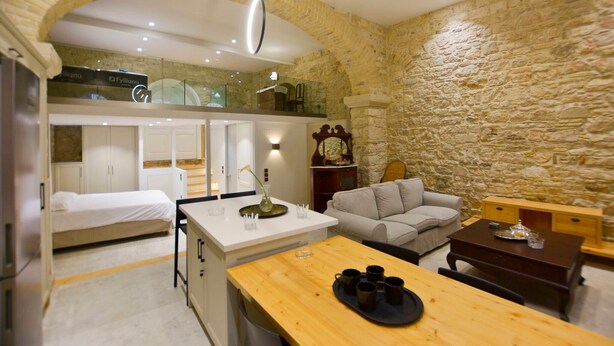 Una habitación de hotel compacta con kitchenette, zona de comedor, sofá y pared de piedra.