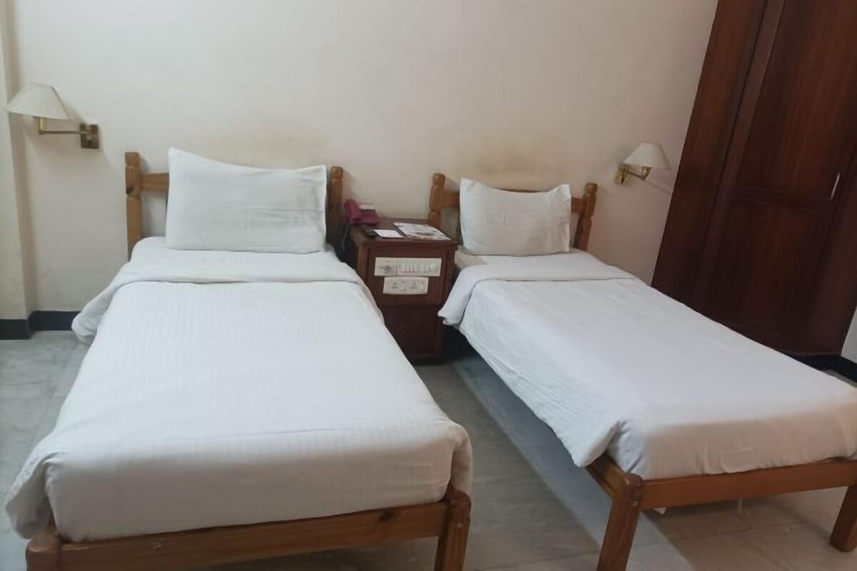 A room with two single beds, wooden headboards, white bedding, a nightstand with a lamp, and a wooden wardrobe.