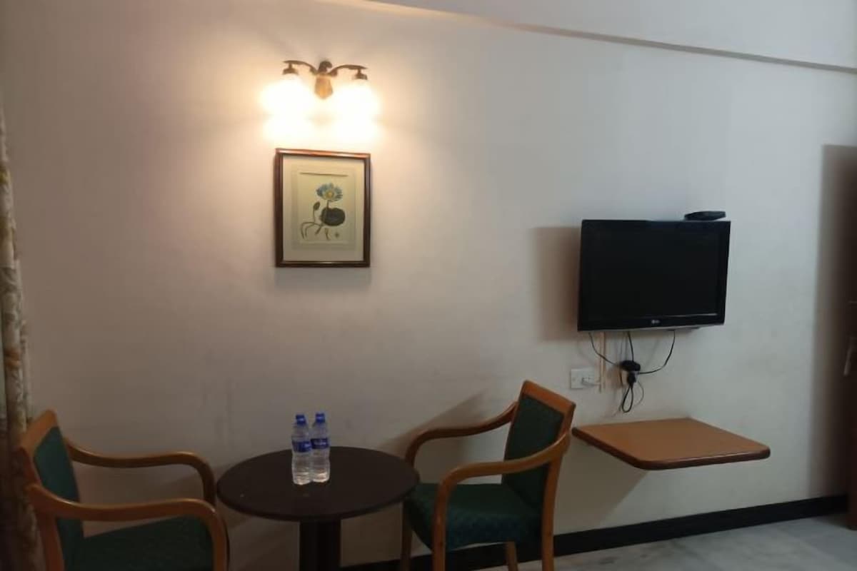 A small room with two wooden chairs, a round table with water bottles, a framed picture on the wall, and a mounted TV.