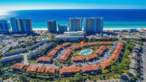 An aerial view of a resort with a central pool, surrounded by hotel buildings and a beach. - MerSea Beaucoup @ Gulf Highlands Sleeps 6 (Panama City Beach)