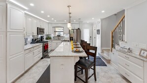 A modern kitchen with white cabinetry, a central island, stainless steel appliances, and a dining area with chairs. - MerSea Beaucoup @ Gulf Highlands Sleeps 6 (Panama City Beach)