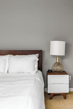 A bed with white bedding, a nightstand with a lamp, and a wall with a switch. - Stylish Palm Springs Retreat with Pool (Palm Springs)