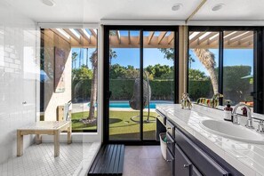 A modern bathroom with a large window, a wooden bench, a sink, and a shower area.