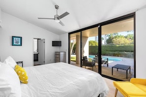 A bedroom with a bed, a TV, a ceiling fan, and a sliding glass door leading to a pool area.