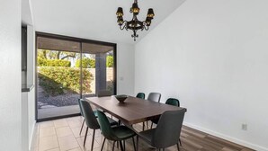 Uma área de refeições moderna com mesa de madeira, seis cadeiras e um lustre.
