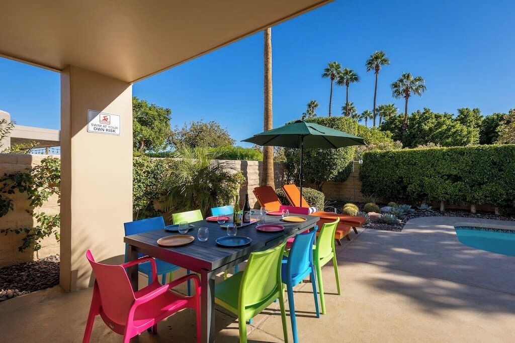 Un área de comedor al aire libre con piscina, sillas de colores y un letrero que indica natación bajo su propia responsabilidad.