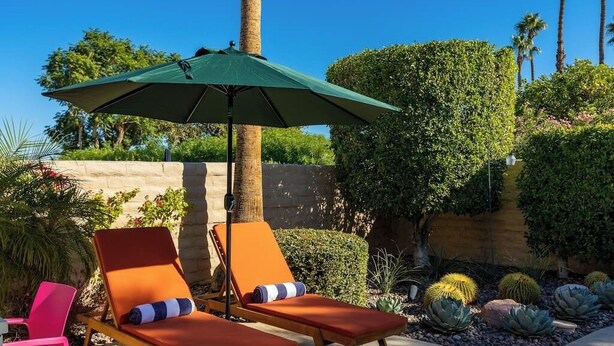 A patio area with two lounge chairs, a green umbrella, and a variety of cacti and shrubs. - Stylish Palm Springs Retreat with Pool (Palm Springs)