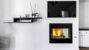 A modern living room with a fireplace, a mounted flat-screen TV, and a minimalist shelf with decorative items. - Stylish Palm Springs Retreat with Pool (Palm Springs)