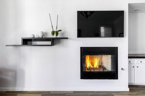 A modern living room with a fireplace, a mounted flat-screen TV, and a minimalist shelf with decorative items.