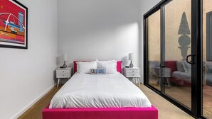 A bedroom with a bed, two bedside tables, a nightstand, a large window with a view, and a framed picture on the wall. - Stylish Palm Springs Retreat with Pool (Palm Springs)